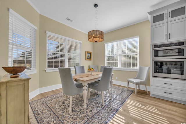 dining room with baseboards, visible vents, light wood finished floors, and ornamental molding