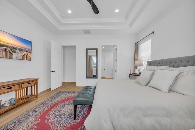 bedroom with visible vents, ornamental molding, a tray ceiling, wood finished floors, and baseboards