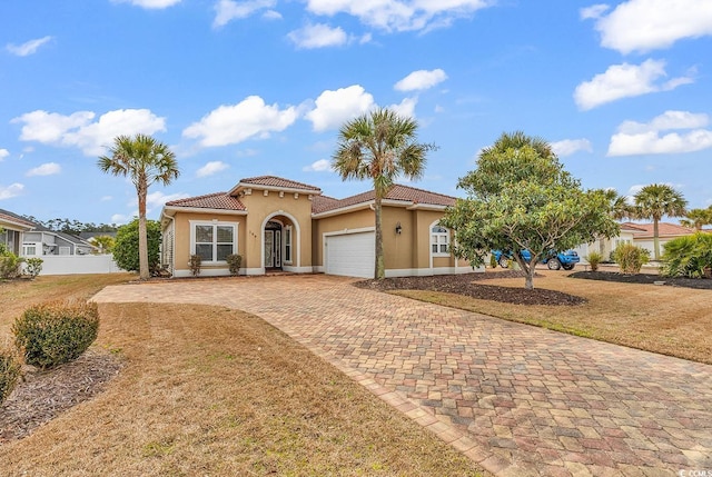 mediterranean / spanish home with a tiled roof, a front yard, stucco siding, decorative driveway, and an attached garage