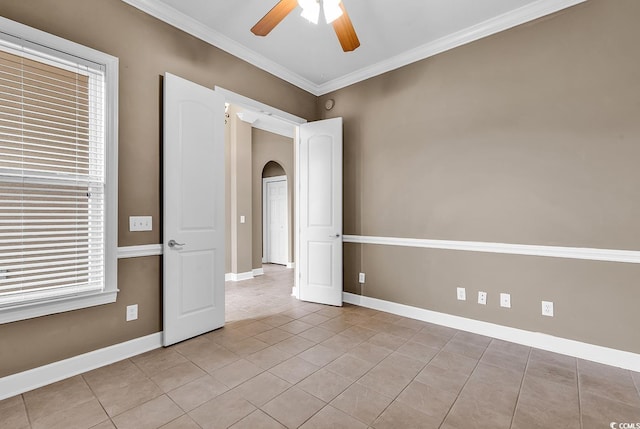 tiled empty room featuring crown molding, a ceiling fan, arched walkways, and baseboards