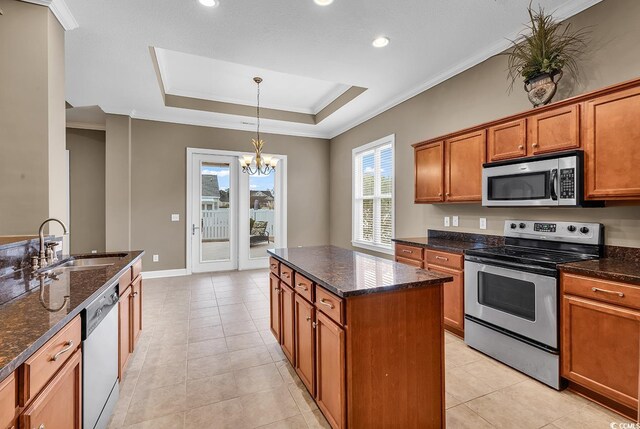 kitchen featuring stainless steel appliances, a sink, brown cabinetry, a raised ceiling, and a chandelier