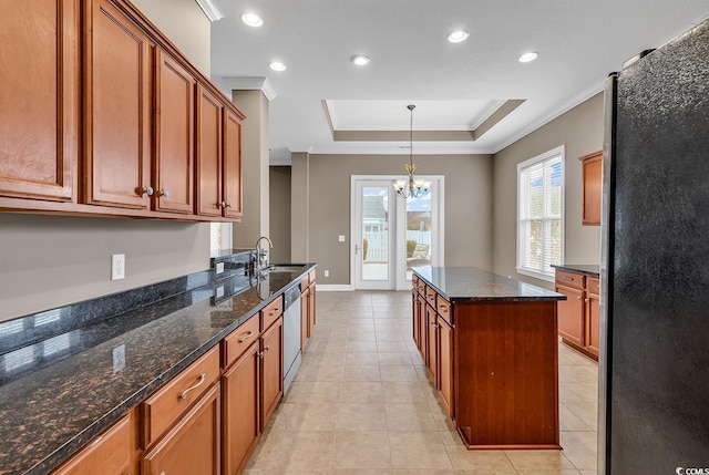 kitchen featuring stainless steel appliances, a raised ceiling, a sink, a chandelier, and brown cabinetry