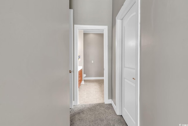 hall featuring light colored carpet, light tile patterned floors, and baseboards
