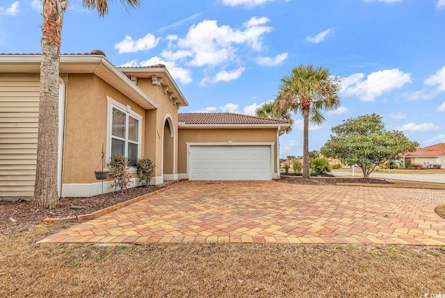 view of side of property featuring stucco siding, decorative driveway, a garage, and a tiled roof