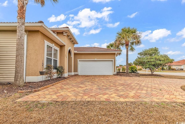 view of side of home with driveway, stucco siding, a garage, and a tiled roof