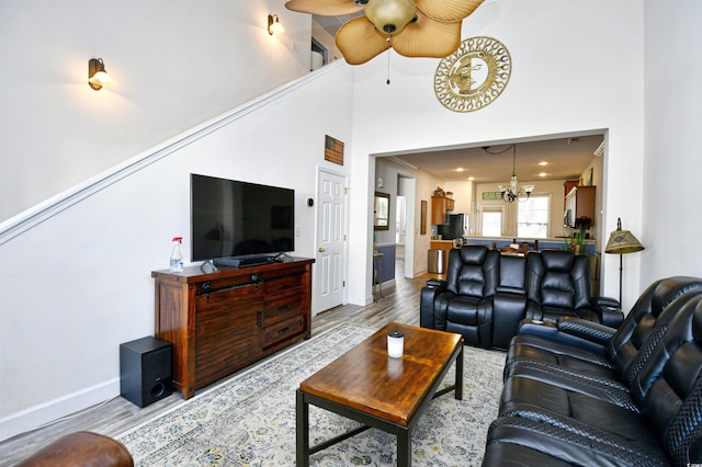 living room featuring ceiling fan with notable chandelier, baseboards, light wood-type flooring, and a towering ceiling