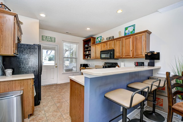 kitchen featuring brown cabinets, black appliances, a breakfast bar, a peninsula, and light tile patterned floors