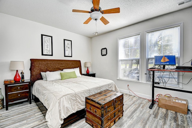 bedroom with visible vents, baseboards, a textured ceiling, and wood finished floors