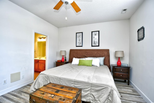 bedroom featuring a textured ceiling, ensuite bathroom, baseboards, and wood finished floors