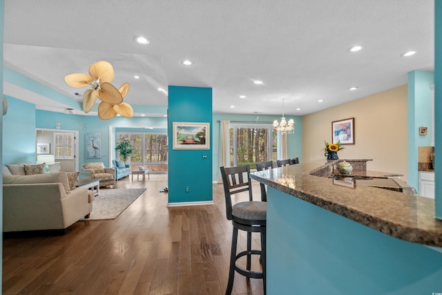 kitchen with a breakfast bar, dark wood-style floors, gas stovetop, recessed lighting, and an inviting chandelier