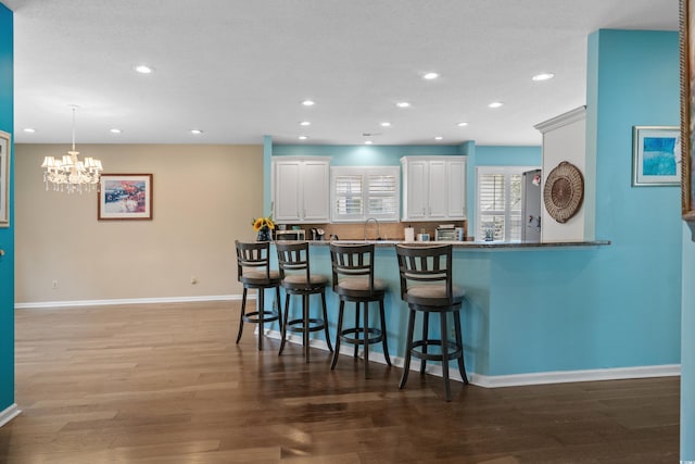 kitchen featuring baseboards, a kitchen breakfast bar, wood finished floors, white cabinets, and a sink