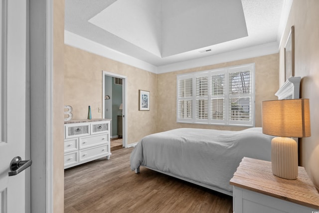 bedroom featuring a tray ceiling, wood finished floors, visible vents, and ornamental molding