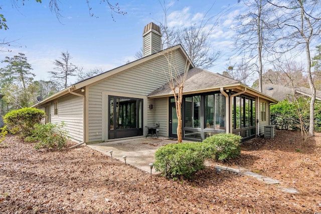 back of house featuring a patio area, a chimney, a sunroom, and a shingled roof