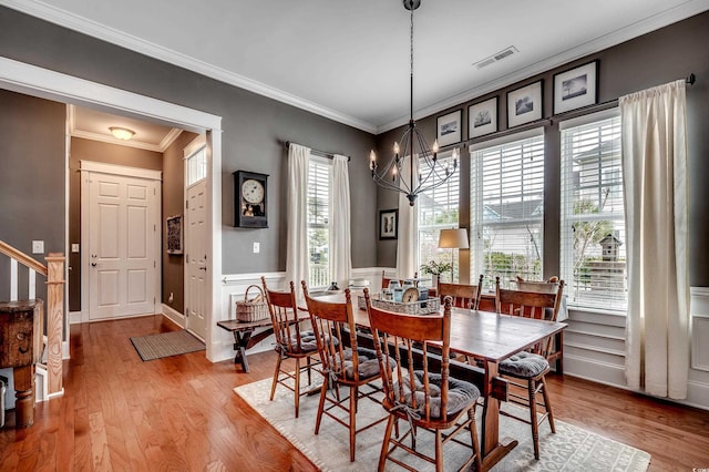 dining room featuring wood finished floors, visible vents, an inviting chandelier, ornamental molding, and wainscoting