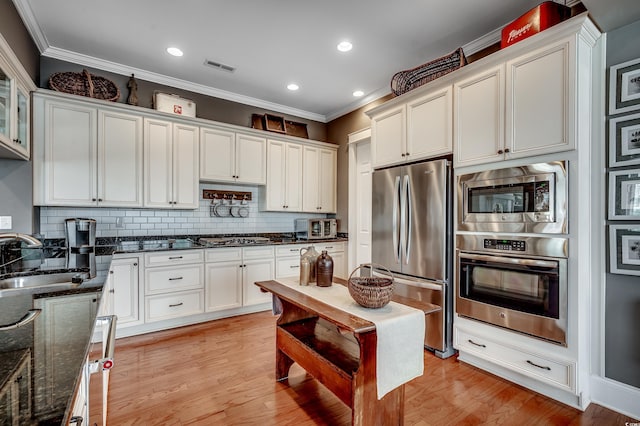 kitchen featuring a sink, appliances with stainless steel finishes, dark stone countertops, and crown molding