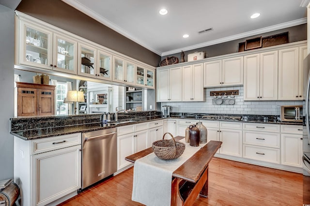 kitchen with visible vents, a sink, stainless steel appliances, glass insert cabinets, and crown molding