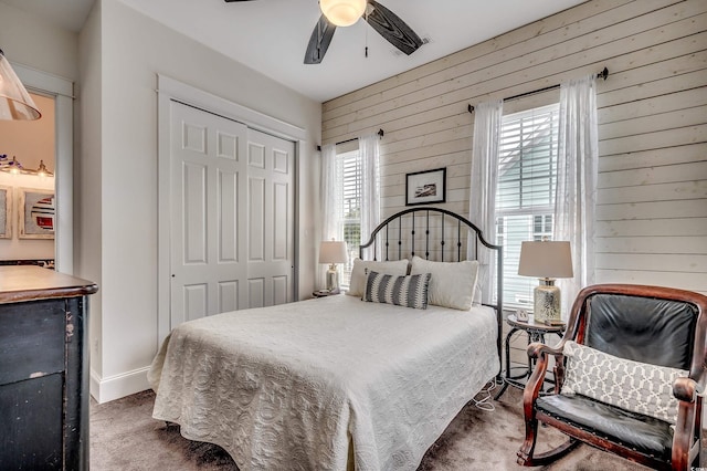 carpeted bedroom featuring a closet, baseboards, wooden walls, and ceiling fan