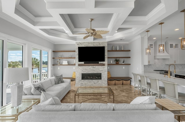 living area with a stone fireplace, coffered ceiling, a ceiling fan, and ornamental molding