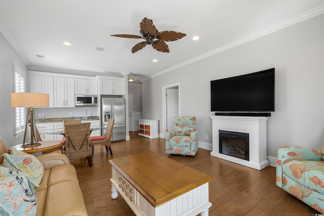 living area featuring dark wood-type flooring, baseboards, ornamental molding, a fireplace, and a ceiling fan