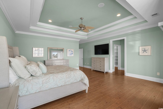 bedroom with visible vents, a tray ceiling, wood finished floors, crown molding, and baseboards