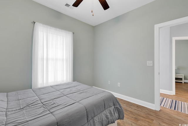 bedroom featuring a ceiling fan, wood finished floors, visible vents, and baseboards