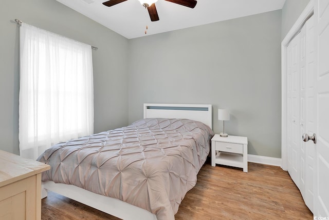 bedroom with light wood-type flooring, a closet, baseboards, and ceiling fan