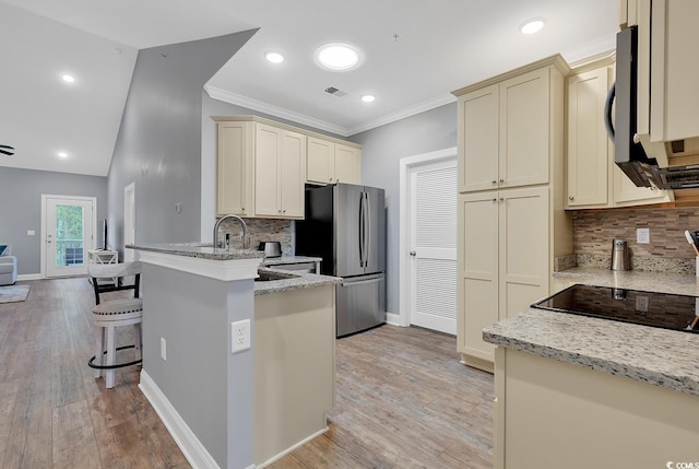 kitchen with visible vents, light stone countertops, a peninsula, cream cabinets, and freestanding refrigerator