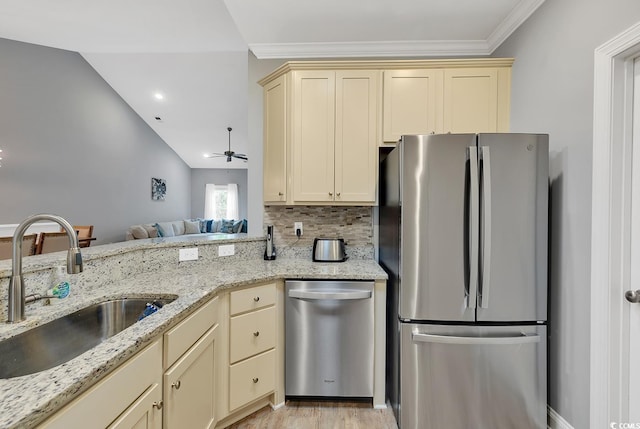 kitchen with light stone countertops, decorative backsplash, appliances with stainless steel finishes, cream cabinetry, and a sink