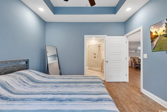 bedroom with ensuite bath, baseboards, a tray ceiling, and wood finished floors