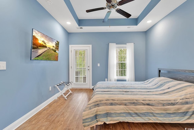 bedroom with visible vents, baseboards, a tray ceiling, wood finished floors, and access to outside