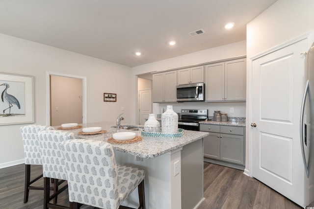 kitchen featuring gray cabinets, appliances with stainless steel finishes, a sink, dark wood-style floors, and a breakfast bar area
