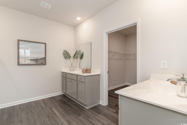 full bath with wood finished floors, two vanities, baseboards, a walk in closet, and recessed lighting