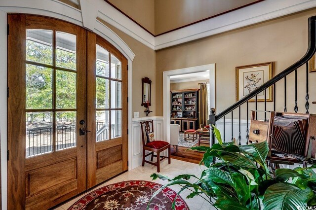 foyer entrance with stairway, a decorative wall, french doors, and wainscoting