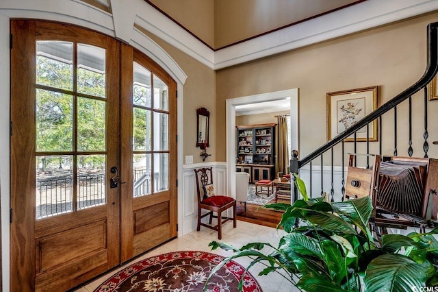 foyer entrance with stairway, a decorative wall, french doors, and wainscoting