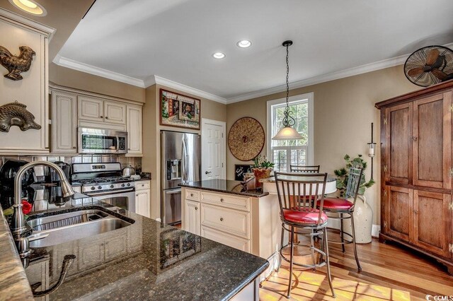 kitchen with ornamental molding, cream cabinetry, appliances with stainless steel finishes, and a sink