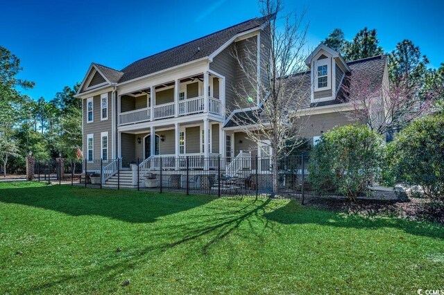 view of front of property with a front yard, a balcony, a ceiling fan, and fence