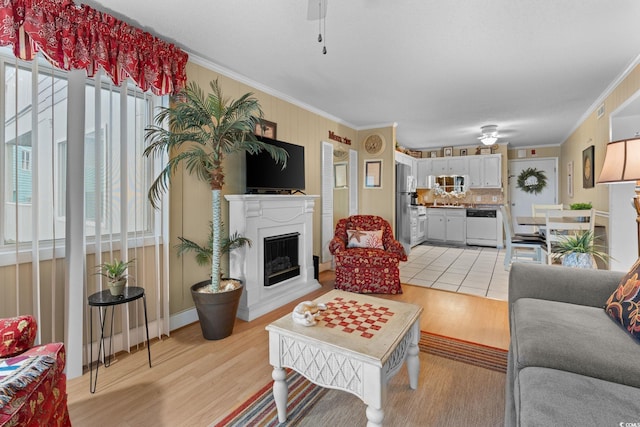 living area with ceiling fan, a fireplace with raised hearth, crown molding, and light wood finished floors