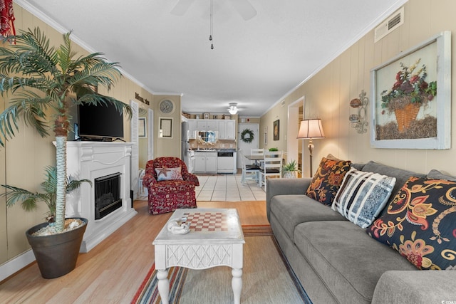 living area with visible vents, a fireplace with raised hearth, crown molding, and light wood-style floors