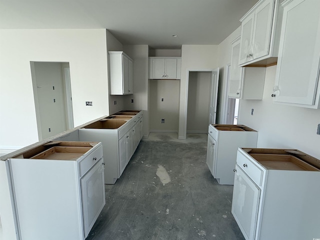 kitchen with white cabinetry, unfinished concrete flooring, and a sink