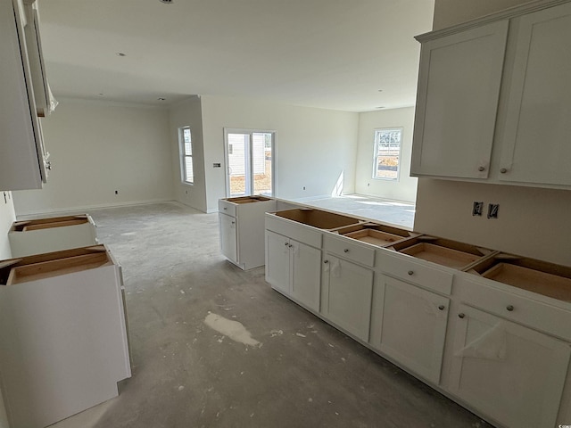 kitchen with a sink, open floor plan, unfinished concrete floors, and white cabinetry