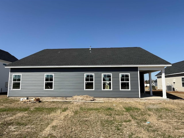 rear view of property featuring central air condition unit, a shingled roof, and a yard