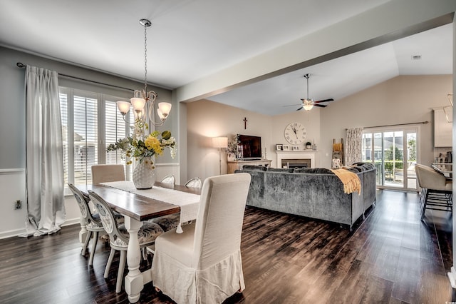 dining room with ceiling fan with notable chandelier, dark wood finished floors, a fireplace, baseboards, and vaulted ceiling