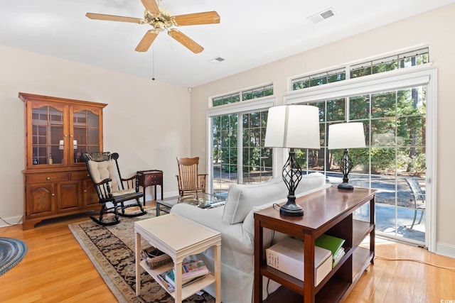 living area with baseboards, visible vents, a ceiling fan, and light wood-style floors