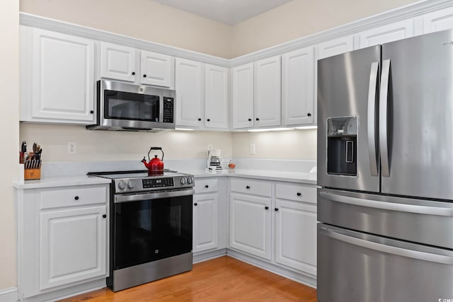 kitchen with light wood finished floors, appliances with stainless steel finishes, white cabinetry, and light countertops