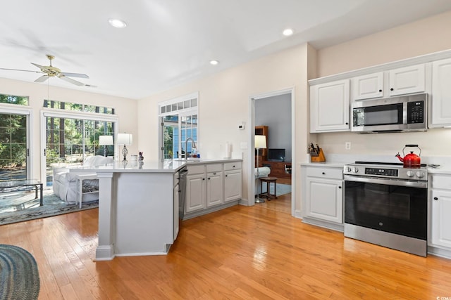 kitchen with a peninsula, light countertops, white cabinets, appliances with stainless steel finishes, and light wood-type flooring