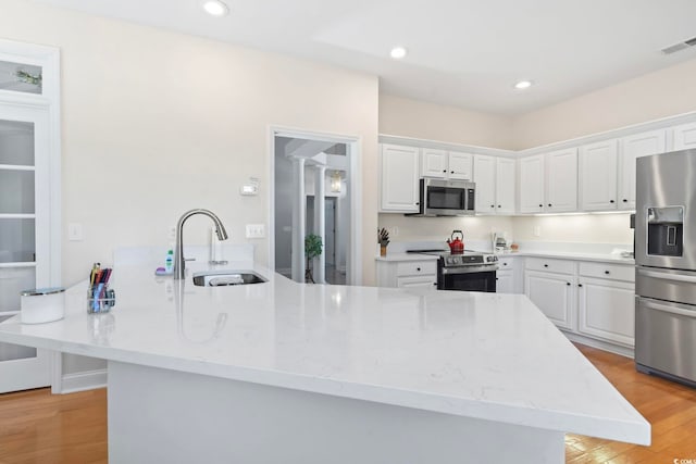 kitchen featuring visible vents, a sink, white cabinetry, stainless steel appliances, and light wood-style floors