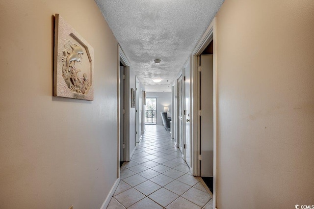 hallway featuring light tile patterned flooring, a textured ceiling, and baseboards