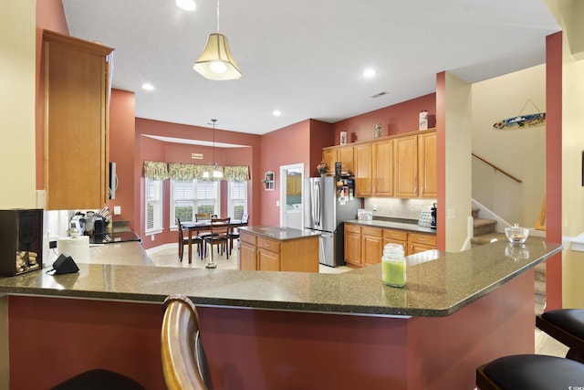 kitchen featuring a breakfast bar, dark stone countertops, backsplash, freestanding refrigerator, and a peninsula