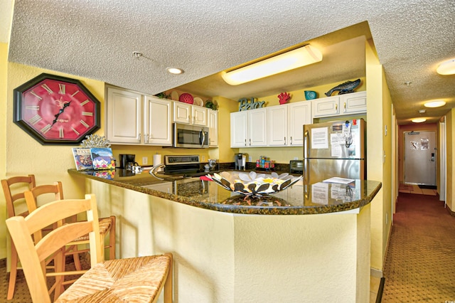 2007 S Ocean Blvd Unit 1106, Myrtle Beach, SC 29577 - kitchen with appliances with stainless steel finishes, a textured ceiling, a peninsula, white cabinetry, and dark stone counters