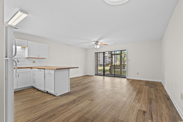 kitchen with a peninsula, white cabinets, light wood finished floors, and white appliances